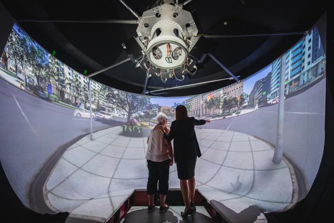 Two people stand in the middle of a curved screen displaying a city street