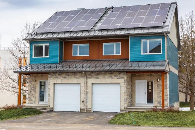 Front-exterior view of side-by-side semi-detached houses, with siding and stone veneer cladding, and solar panels on the roof.