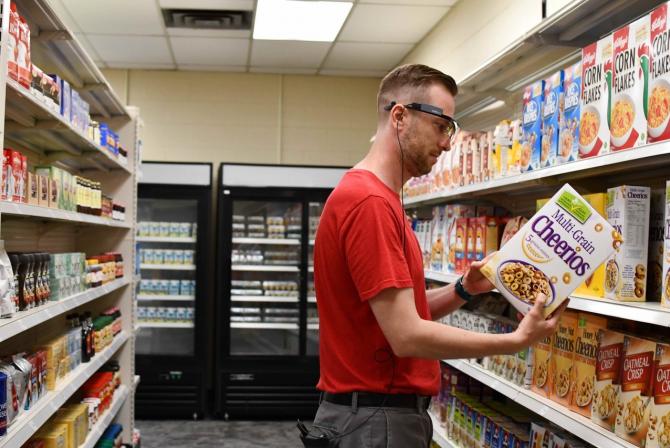 Une personne dans une allée d'épicerie porte des lunettes et examine le côté d'une boîte de céréales Cheerios