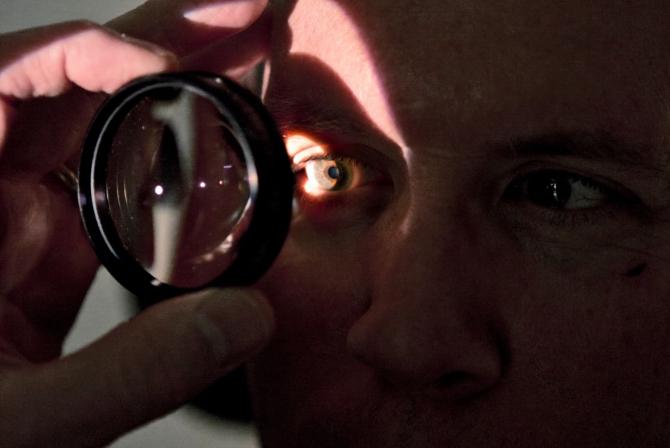 Close up of a person holding a lens in front of their right eye