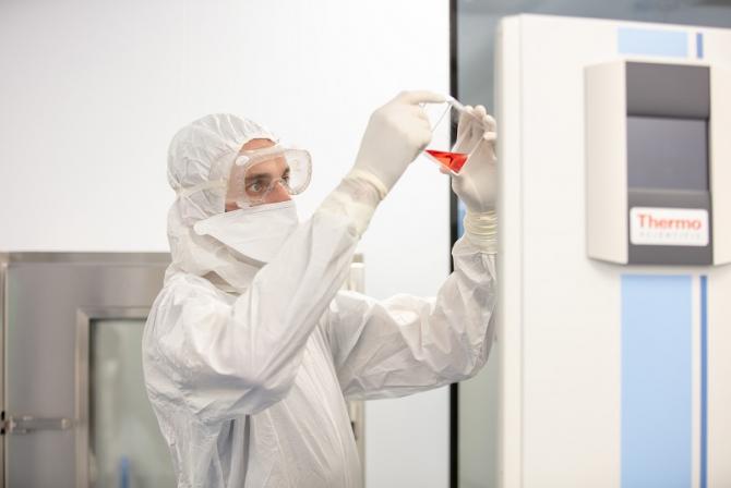 Une personne portant de l'équipement de protection individuelle inspecte un liquide à travers une boîte transparente