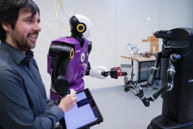 Une personne utilise une tablette électronique pour manipuler deux robots