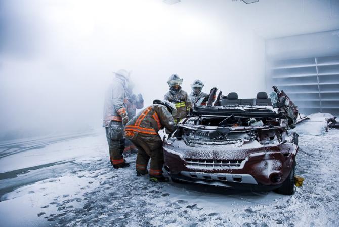 Une équipe de pompiers travaille sur une voiture très endommagée dans une salle d'essai couverte de neige