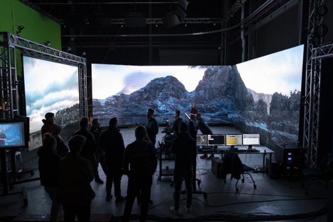 Group of people face a large 3-sided screen displaying mountain tops