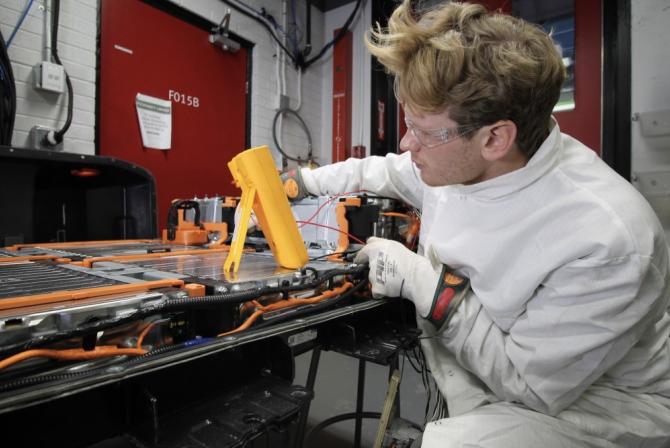 A person dressed in protective gear uses equipment to test battery packs.