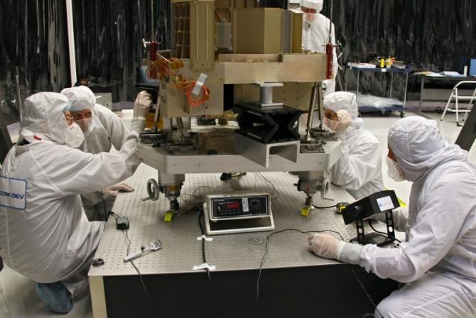 The Fine Guidance Sensor engineering test unit sits on an elevated platform surrounded by lab technicians 