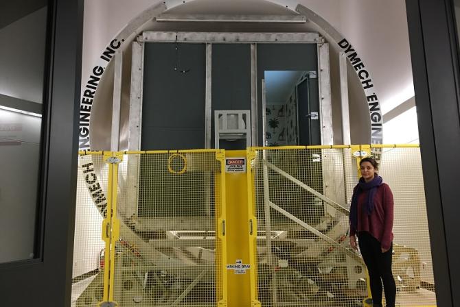 Person stands in front of a yellow gate blocking entry to a large circular gateway leading to a room beyond.