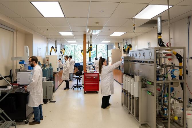 People wearing lab coats work at various stations in a lab.