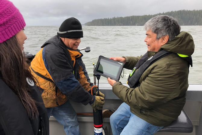 People aboard a boat look at data displaying on a tablet.