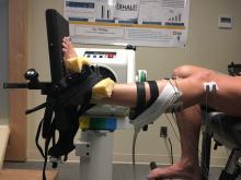 Leg device set-up where subject sits in a chair with electrodes and measurement devices attached the raised left leg and foot 