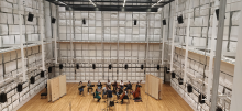 Un orchestre joue dans une grande salle où les murs sont couverts de panneaux et de haut parleurs