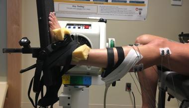Leg device set-up where subject sits in a chair with electrodes and measurement devices attached the raised left leg and foot 