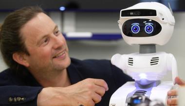 Un chercheur interagit avec un petit robot doté d’intelligence artificielle.